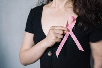 Woman in a black button-front top holding a pink breast cancer awareness ribbon at her chest, for an article debunking myths about nipple covers and breast cancer