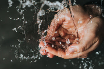 Water splashing over cupped hands under a running tap, for a guide to washing and caring for reusable silicone nipple covers and nipple pasties