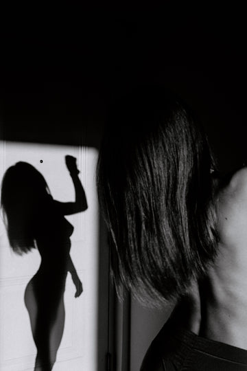 Black-and-white photo of a woman with her back turned and her silhouette cast on a white wall, for a nipple cover hack on hiding your nipples without wearing a bra
