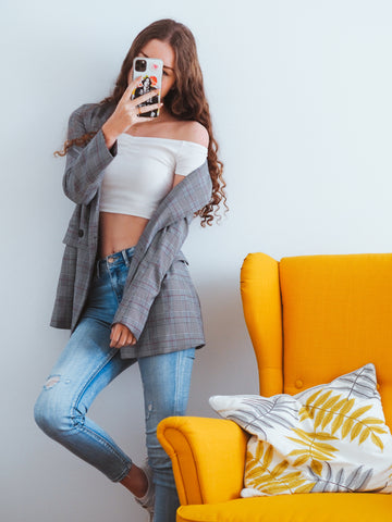 Woman in a white off-the-shoulder crop top, grey blazer and ripped jeans taking a mirror selfie, for a step-by-step guide to applying silicone nipple covers the right way