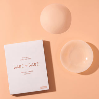 Adhesive Nipple Covers in Creme: two round reusable silicone nipple covers, one turned to show its sticky adhesive side, next to the Bare Babe invisible nipple covers box in medical-grade silicone.