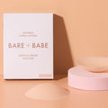 Non-Adhesive Nipple Covers in Creme: two round, non-sticky reusable silicone nipple covers, one on a pink stand and one dome-side up, beside the Bare Babe medical-grade silicone box.