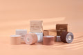 Boob Tape Kit lineup: four rolls of invisible breast lift tape in four of the five shades, Creme through Mocha, standing in front of their Bare Babe boxes labeled medical-grade adhesive.