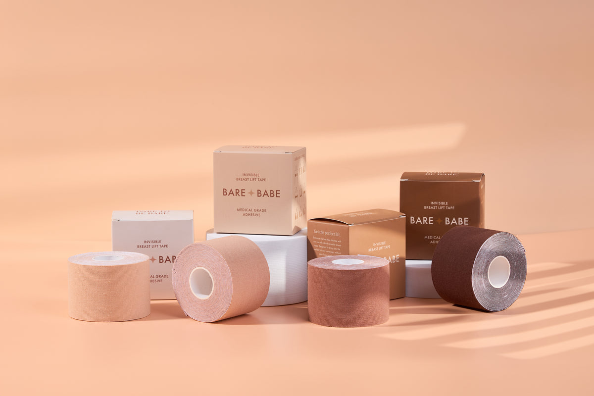 Boob Tape Kit lineup: four rolls of invisible breast lift tape in four of the five shades, Creme through Mocha, standing in front of their Bare Babe boxes labeled medical-grade adhesive.