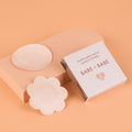 Satin Nipple Pasties box, disposable satin nipple covers, 20 pairs, with one round and one flower-shaped pasty in Creme on a peach backdrop.