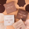 Satin Nipple Pasties boxes in four shades stacked on white display blocks, each holding 20 pairs of disposable satin nipple covers in round and flower shapes.