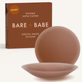 Adhesive Nipple Covers in Cocoa: a pair of round, matte, reusable silicone nipple covers, one tilted to show the sticky side, in front of the Cocoa box marked Sticky and medical-grade silicone.