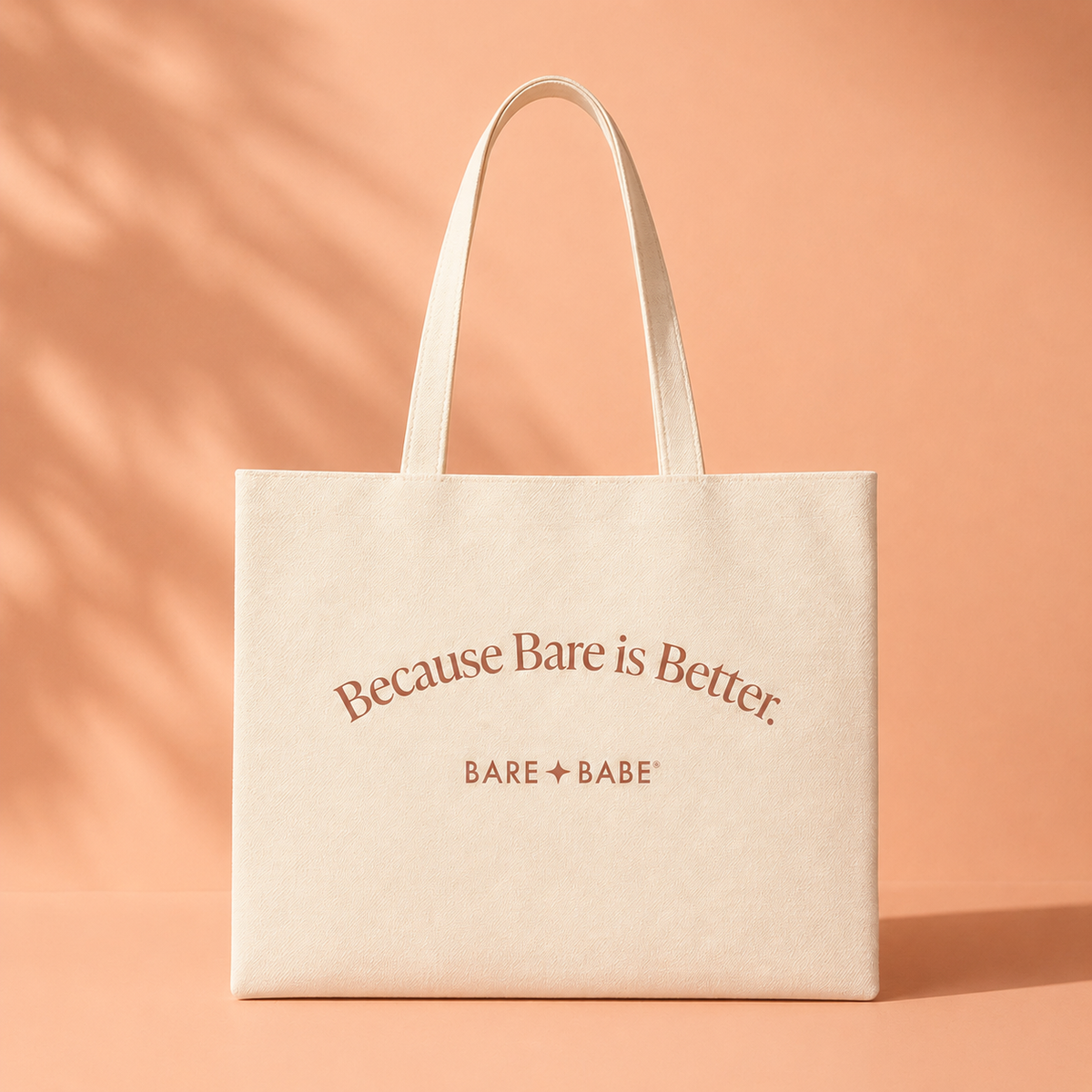 Because Bare is Better Tote Bag, a cream canvas shoulder tote with the "Because Bare is Better." slogan and Bare Babe logo printed in terracotta, on a peach background