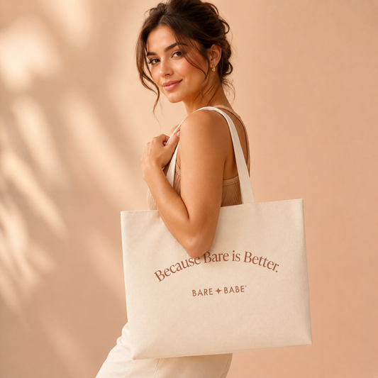 Because Bare is Better Tote Bag, a cream canvas tote printed with "Because Bare is Better." and the Bare Babe logo, carried on the shoulder by a woman in a sleeveless knit top