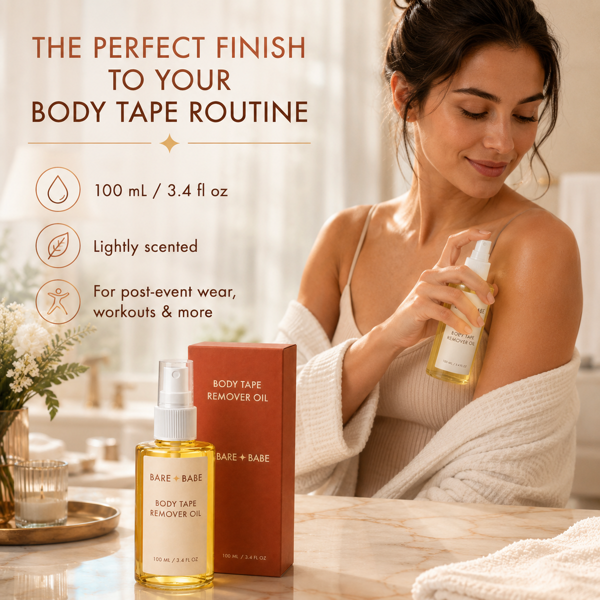 Boob Tape Remover Oil in use: a woman in a cream robe sprays the oil onto her shoulder at a marble vanity. 100 ml / 3.4 fl oz, lightly scented, for taking off body tape after events, workouts and more, on intact skin.