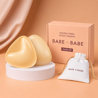 Extra-Boost Sticky Push Up Inserts in Honey, a pair of double-sided sticky push-up bra inserts on a pedestal beside the Bare Babe Push Up box and a white drawstring travel bag
