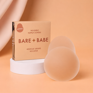 Easy Lifting Nipple Covers (One Tab): a pair of single-tab reusable silicone nipple covers beside a Lifting invisible nipple covers box in medical-grade silicone, on a white pedestal against a peach backdrop