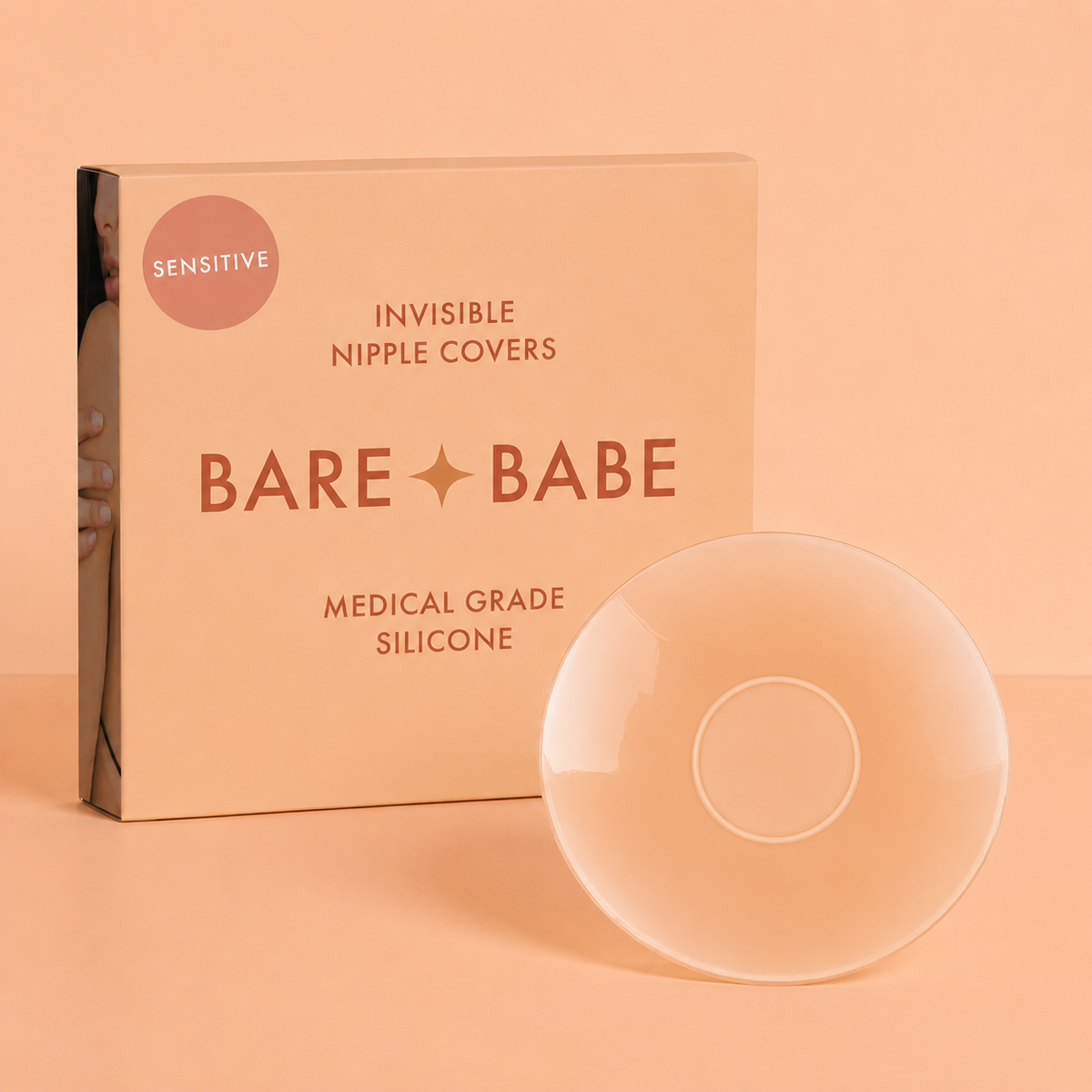 Sensitive Adhesive Nipple Covers: a round sticky silicone nipple cover turned to show its adhesive-free center ring, standing beside the Bare Babe Sensitive invisible nipple covers box in medical-grade silicone.